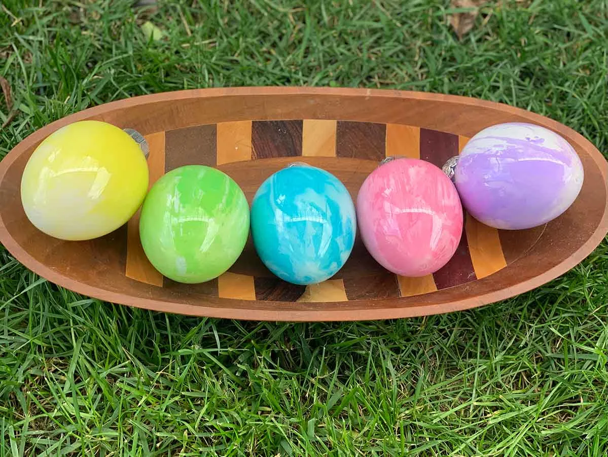 Five Pouring Paint Easter Eggs in a wooden bowl showing color and design variations