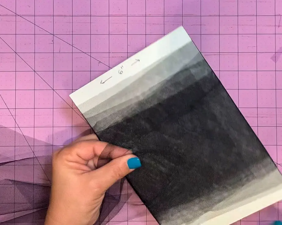 6" wide and about 8" wide piece of cardboard with a strip of 6" wide tulle being wrapped around the cardboard to facilitate cutting tulle squares.