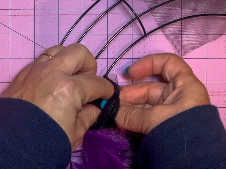 Two hands tying slip knot out of tulle to attach the tulle to a wreath form. The tail of the tulle is being slipped through the loop.