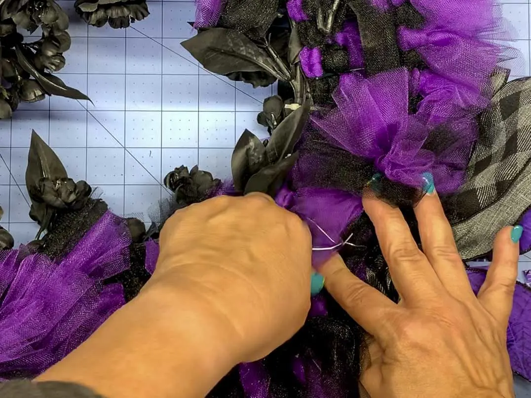 Attaching a bow to a wreath by wrapping the wire around the wreath form and twisting the ends together.