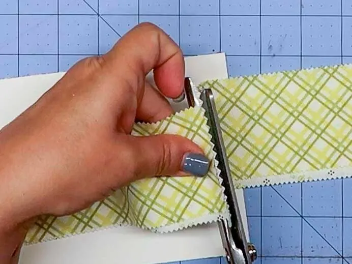 Hands cutting an 8" piece of fabric from a longer strip with pinking shears.