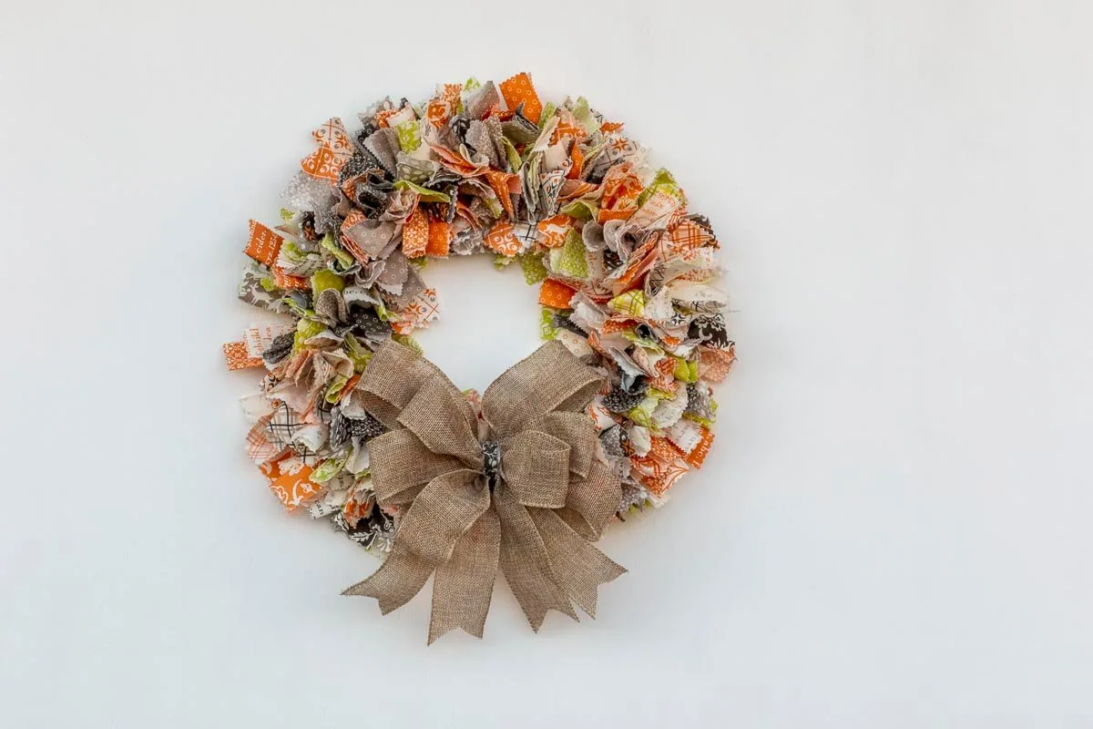 Fabric wreath made of multi-colored and multi-patterned strips of fabric with a large burlap bow at the bottom of the wreath.