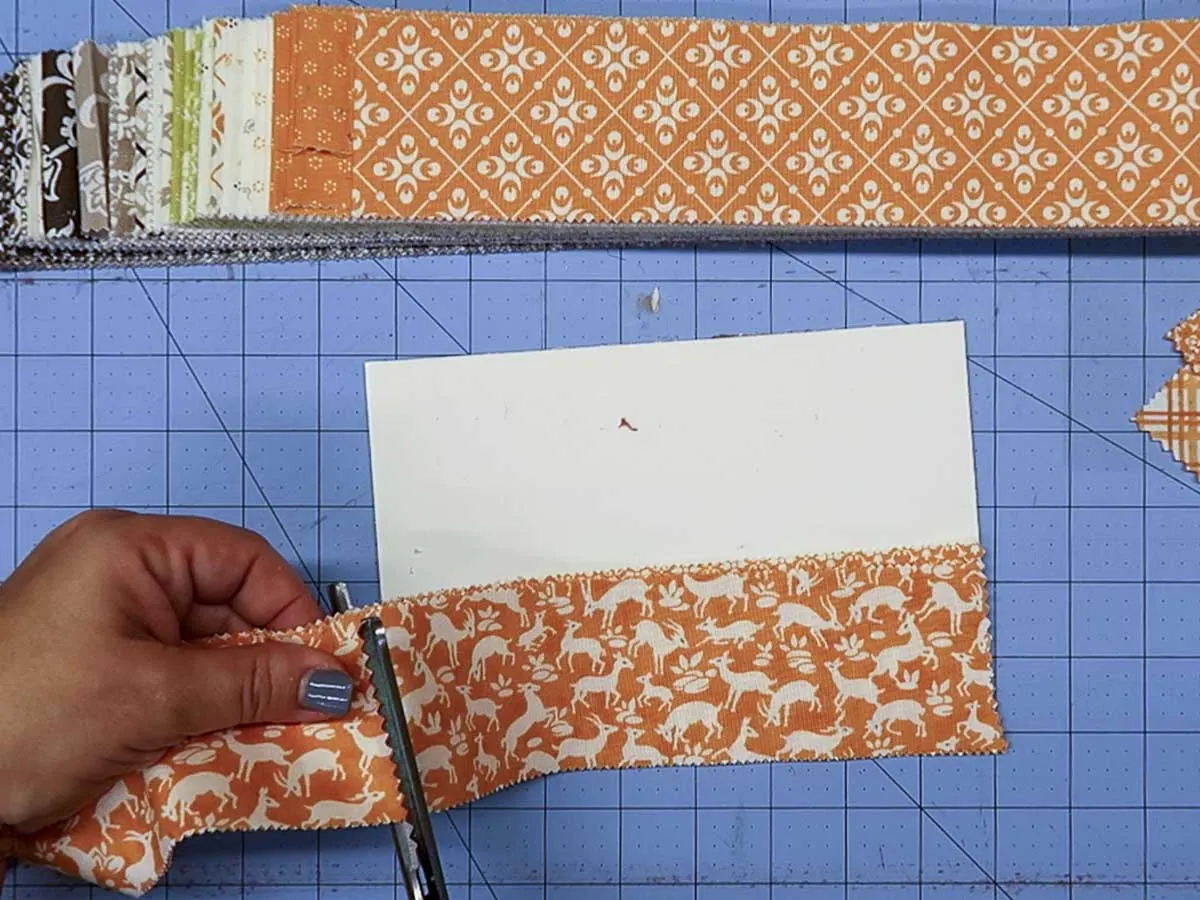 Hands cutting an 8" piece of fabric from a longer strip with pinking shears.