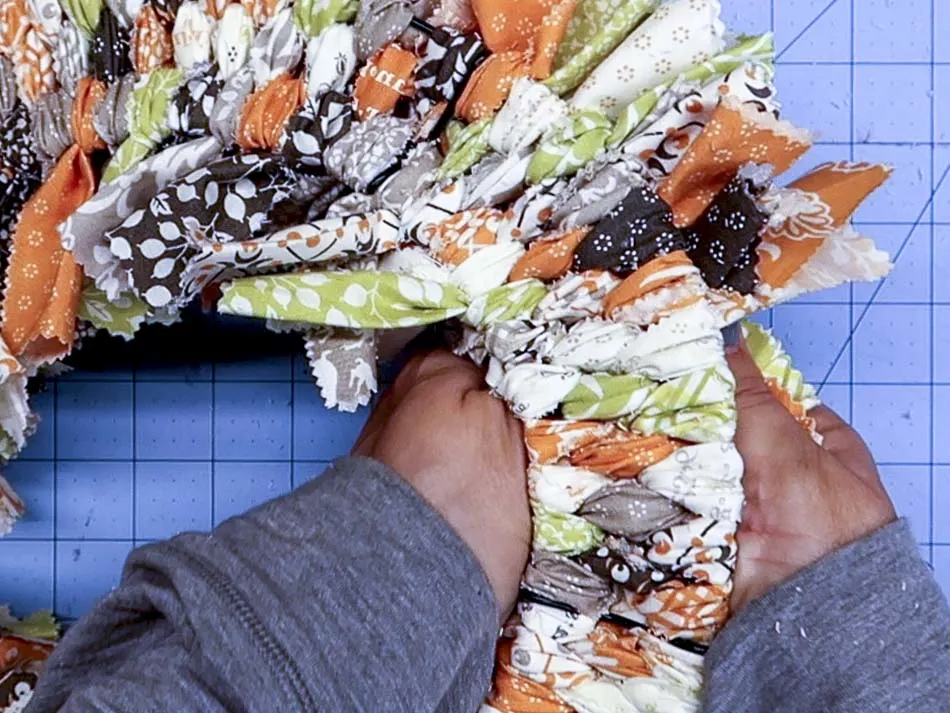 Handing showing the reverse side of the rag wreath.Some of the knots have been fixed so the ends of the fabric face the front of the wreath.