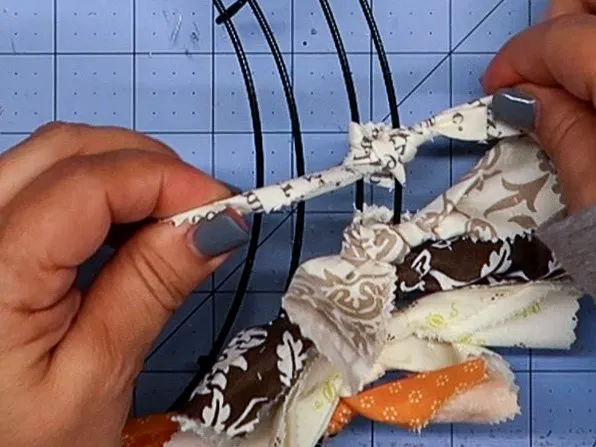 Hands pulling the two ends of a piece of fabric tied in a knot over the two outer rings of a wire wreath form.