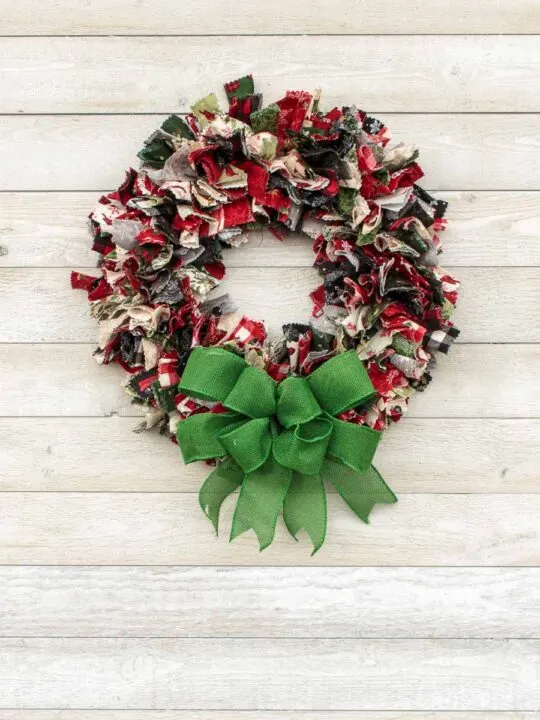 Fabric wreath made of multi-colored and multi-patterned strips of fabric with a large burlap bow at the bottom of the wreath.