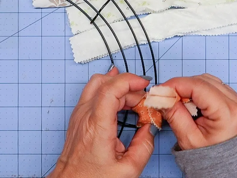 Hands forming a knot with a small piece of fabric over the two outer rings of a wire wreath frame.