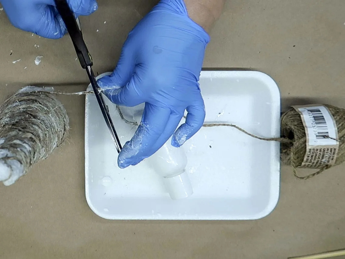 Scissors cutting the glue covered string after wrapping the twine around the cone.