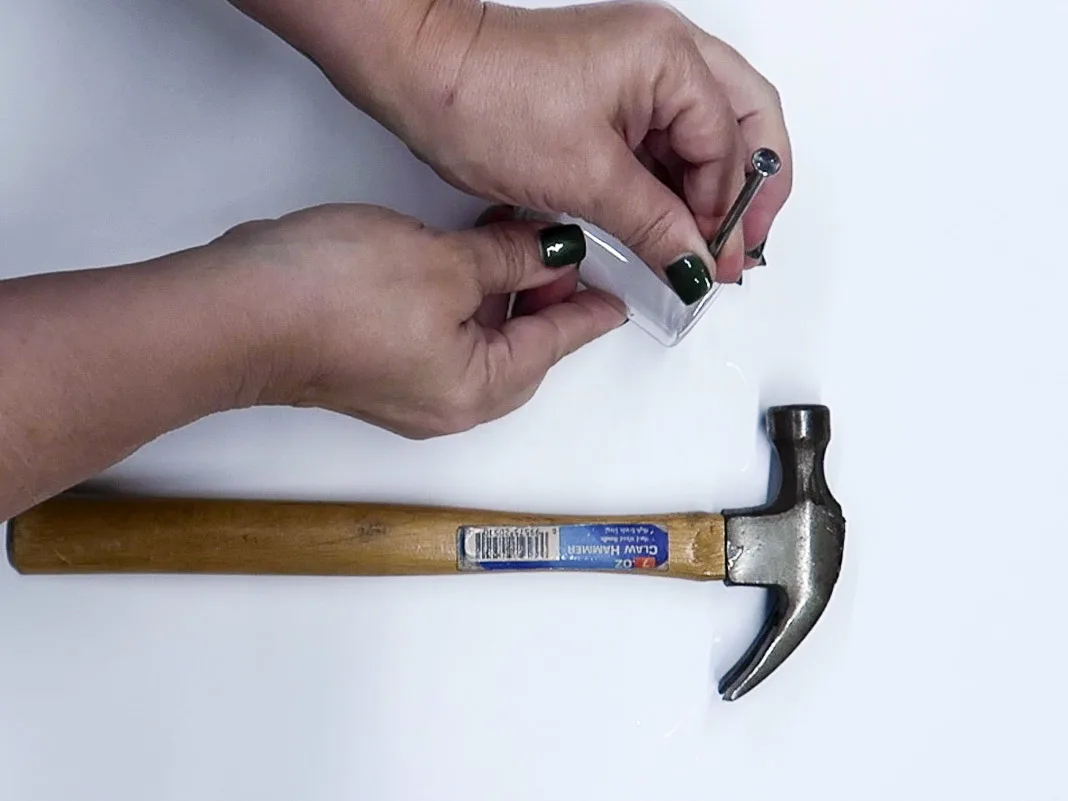 Hand holding a large framing nail to show where to hammer it into a plastic bottle.