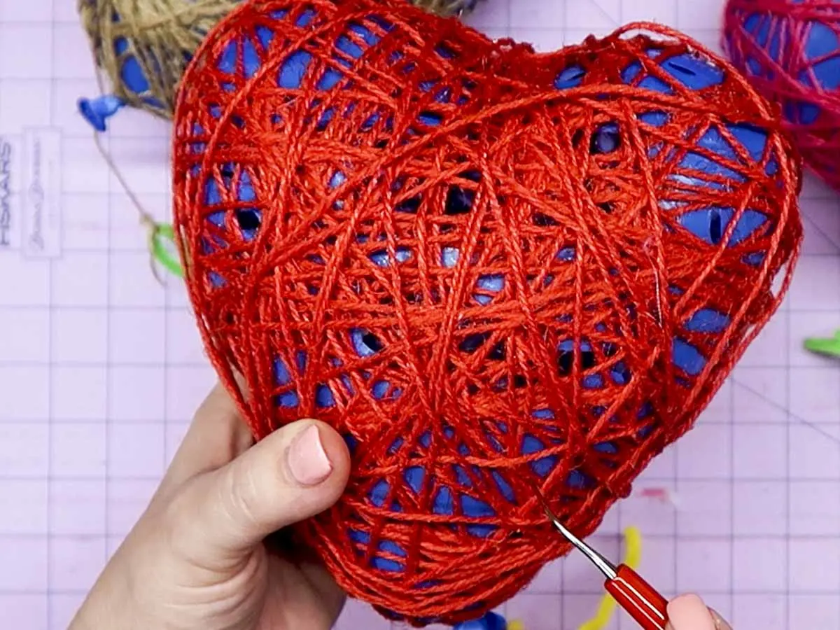 Hands popping holes in the balloon inside a DIY Twine Heart.