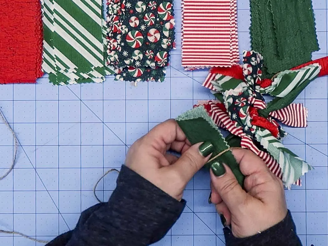 Hands tying a folded piece of fabric to a string to make a fabric garland.