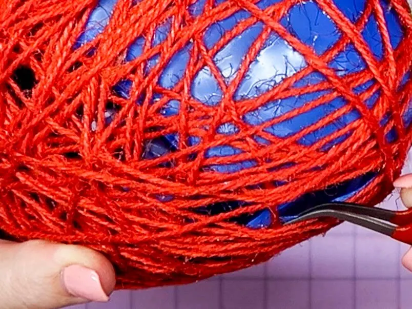 Hands using a tweezer to remove pieces of the popped balloon from the inside of DIY Twine Hearts.