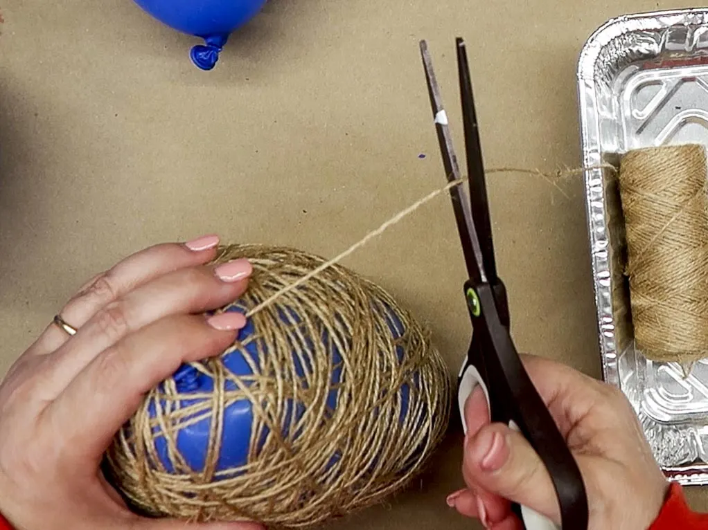 Hands cutting a piece of twine from the roll after wrapping a balloon with the twine.