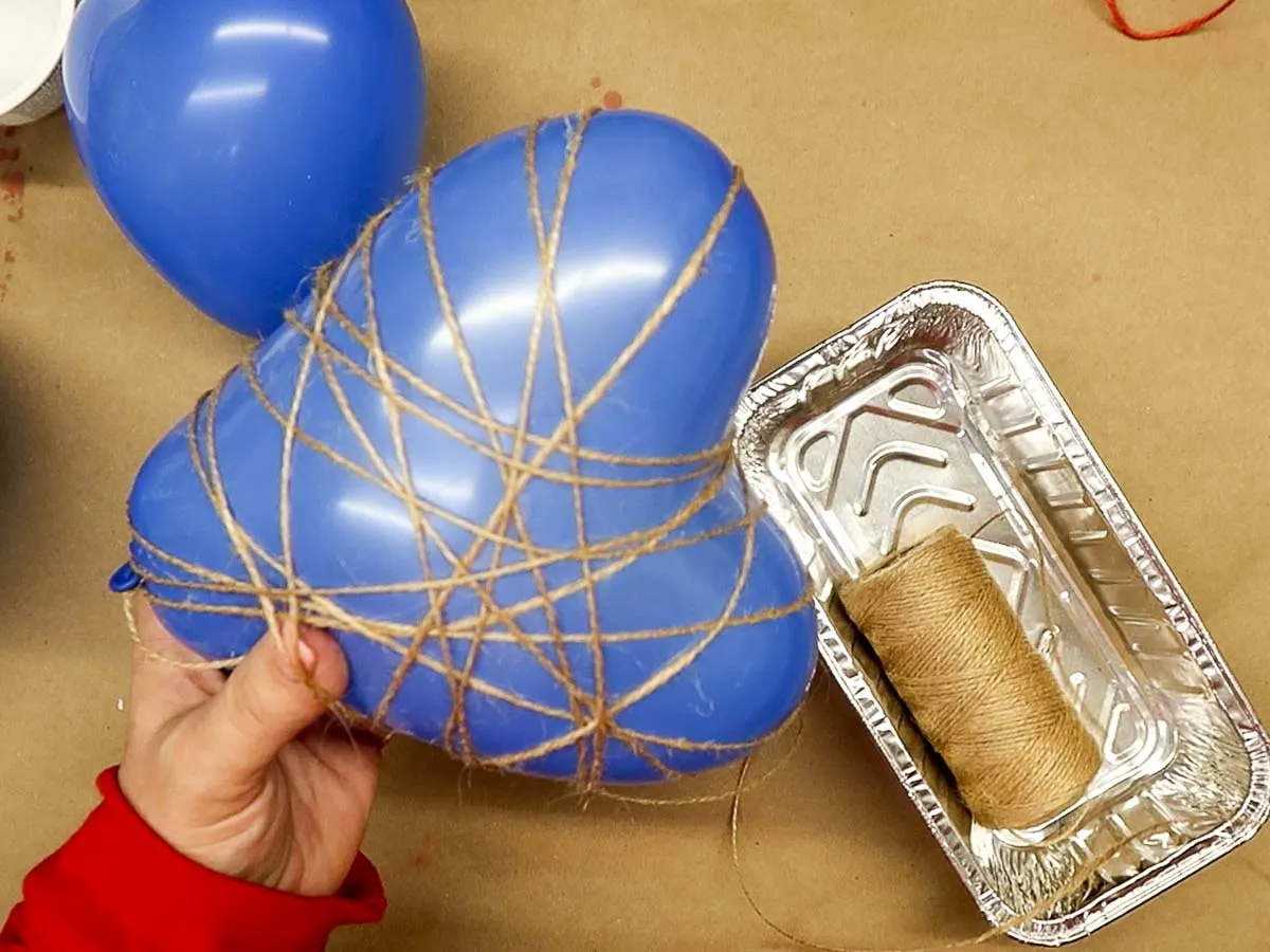 Heart-shaped balloon partially covered with twine from a roll of tan twine.